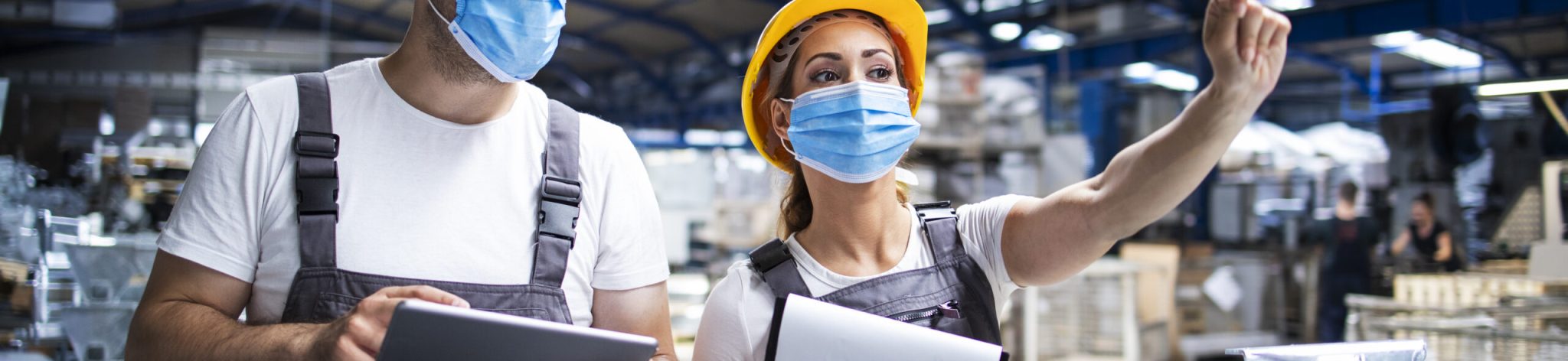 Factory workers with face masks protected against corona virus doing quality control of production in factory.